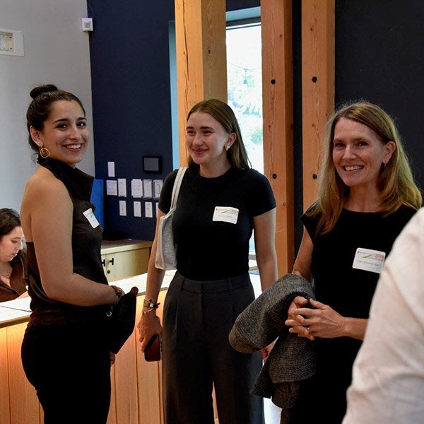 Three people wearing name tags stand together and smile during an indoor event.