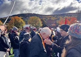 A person wearing a medal bows their head as another person adjusts the ribbon during an outdoor gathering.