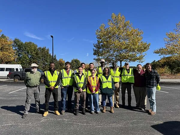A group poses in a parking lot, with several people wearing reflective safety vests.