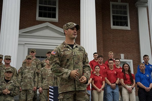 Norwich cadet Martin speaks in front of a group of uniformed cadets and students wearing red and blue shirts outside a brick building.