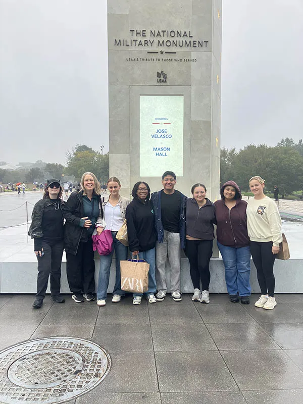 Eight people stand together in front of the National Military Monument on a rainy day.