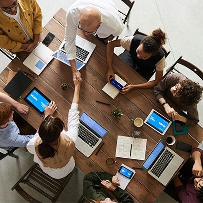 A group of individuals working at a table using laptops and other devices, as seen from above.