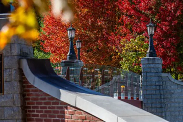 Brick and stone bridge railings with black lanterns stand among red and orange autumn leaves.