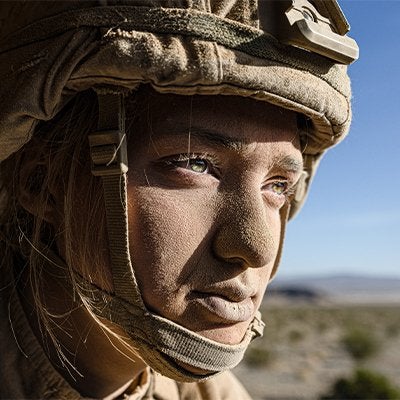 Close-up portrait of a soldier wearing a helmet and protective gear, looking toward the distance in a dry, open landscape.