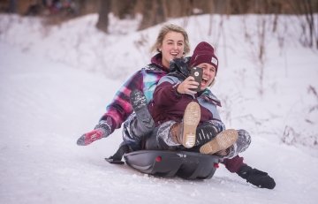 Two students sledding and taking a video selfie