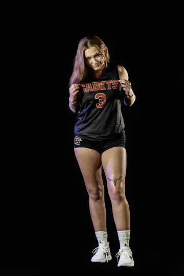 Rae Lawing stands in front of black background while pulling out the "Cadets" name on her jersey.