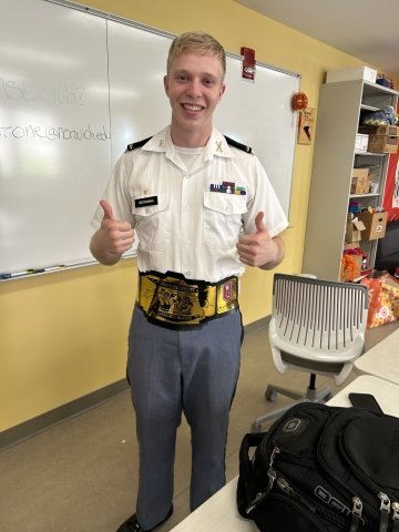 A Norwich University cadet smiles proudly, showing off the gold “Language Slayer” belt for outstanding language achievement.