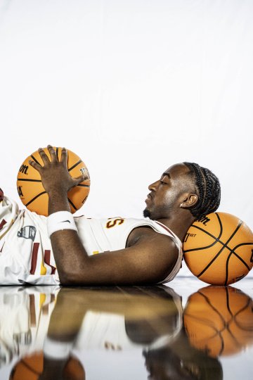 Person in a Norwich University basketball uniform lying on a reflective surface, holding and looking at a basketball.