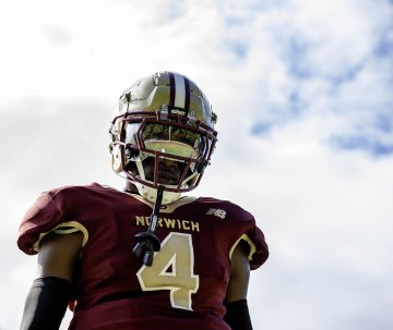 Norwich University football player in maroon and gold uniform and helmet, standing against a cloudy sky.