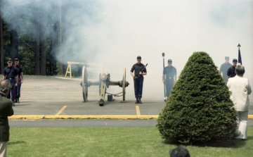 two men facing row of Norwich University cadets, possibly members of the Norwich Independent Battery, firing a cannon