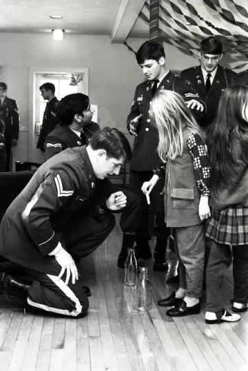 cadet in uniform kneels before two children, with two other cadets in uniform beside them