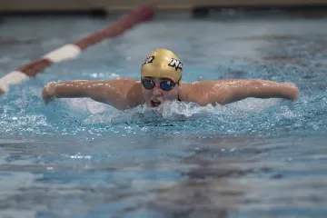Swimmer in a pool performing the butterfly stroke, wearing a cap marked "Norwich" and goggles, in a competitive setting.