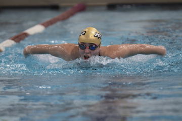 Swimmer in a pool performing the butterfly stroke, wearing a cap marked "Norwich" and goggles, in a competitive setting.