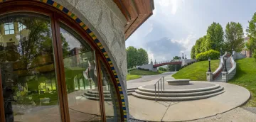 Panoramic view of the exterior of the Sullivan Museum and History Center, featuring a curved glass facade and adjacent outdoor steps leading to a green lawn and distant bridge.