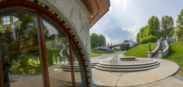 Panoramic view of the exterior of the Sullivan Museum and History Center, featuring a curved glass facade and adjacent outdoor steps leading to a green lawn and distant bridge.