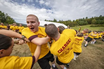 Participants in yellow 'Charge' T-shirts engage energetically in a teamwork activity outdoors.
