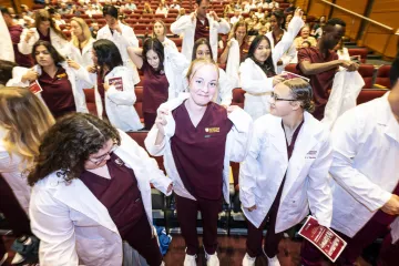 Group of medical students in white coats participating in a ceremony in an auditorium.