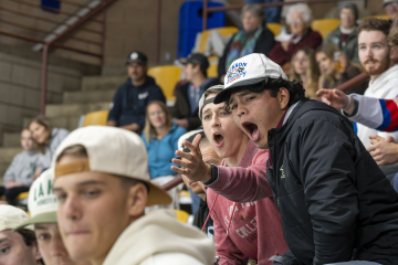 Two excited fans at a sports event, one wearing a 'Madison 1996' cap, enthusiastically cheering in a crowded stadium.