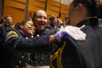 Two joyful cadets in formal military uniforms embracing each other at a ceremonial event.