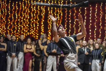 A performer from Norwich University Drill Team performs in front of an audience with a backdrop of sparkling lights.