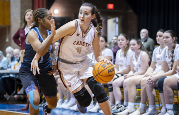 Two basketball players in action during a game, one from the Cadets team dribbling past an opponent.