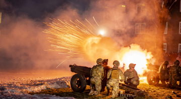 Norwich University cadets conducting a training exercise near a large fire and sparks, with a military cannon in the foreground.