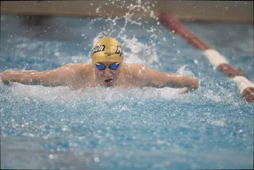 Swimmer in action at a pool wearing a cap with 'Norwich' logo and blue goggles, competing in a butterfly stroke race.