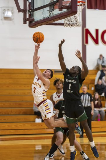 Two basketball players, one in a 'Cadets' jersey and the other in a 'Plymouth' jersey, are jumping near the basket, competing to score during a game. The player in the 'Cadets' jersey is attempting a layup while the 'Plymouth' player attempts to block the shot.