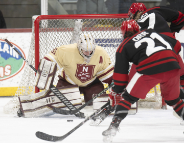 Goalkeeper from Norwich University Hockey makes a save during a hockey game against another player.