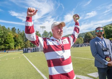 man in striped rugby shirt raising both arms in the air