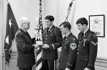 older man in uniform presents trophy to three cadets in uniform