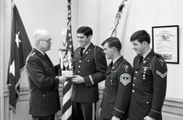 older man in uniform presents trophy to three cadets in uniform