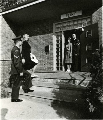 two couples, men in military uniform, women dressed more casually, at entrance of a building with sign "Flint Hall"
