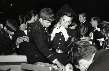two cadets in uniform look at rings on table and in hand