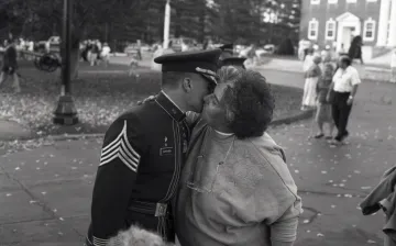 Cadet in uniform embraces woman, people in background walking toward them