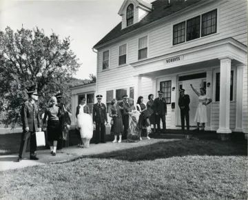 large group of men in military uniform, women in dresses, in front of entrance to building named "Roberts Hall"