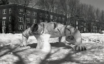 snow sculpture of what appears to be a person doing a pushup with brick buildings in background