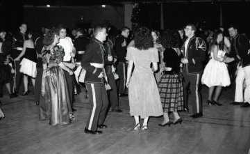 couple in foreground, cadet in uniform with woman from behind in dress, dance in front of a group of other couples