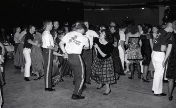 group of students, many seen from behind, dancing on parquet floor