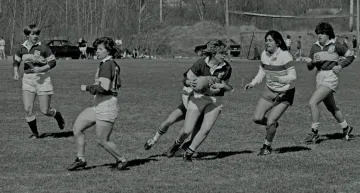 six women rugby players, with center player holding ball