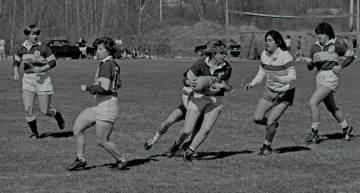 six women rugby players, with center player holding ball
