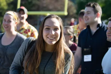 A women smiles as she passes by with other individuals in her class's entrance to football in the Norwich University 2019 Homecoming alumni parade.