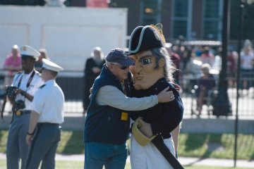Man in blue vest and baseball cap hugs a mascot of Norwich University. Photo of Kurt Buddha Schlotterbeck '66 hugging the Alden Partridge mascot.