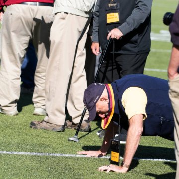 Man in blue vest and baseball cap doing a pushup on football field. Photo of Philip Ackley '66.