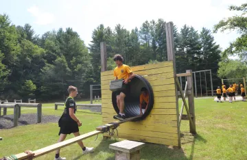 FLC camper walking down a beam as part of the challenge course.