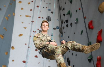 NU student rappelling from rock climbing wall and smiling.