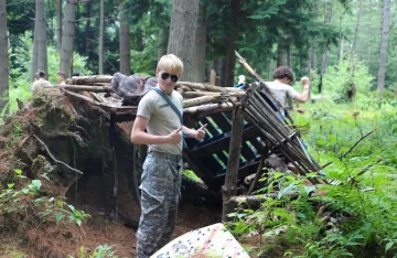 FLC attendee giving thumbs up after completing his shelter in the woods.