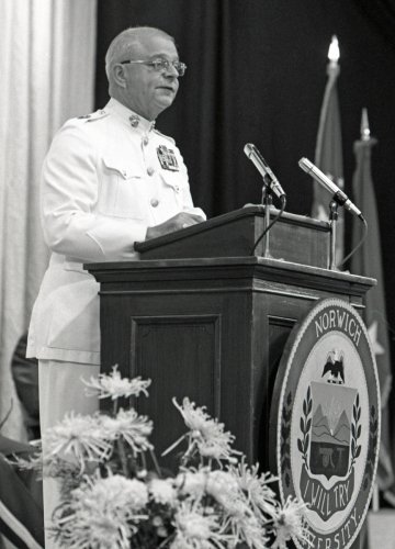 black and white photo of a man in white uniform addressing a crowd from a lectern. Photo is of Herman Poggemeyer Jr. as Commissioning ceremony speaker at norwich university 1976.