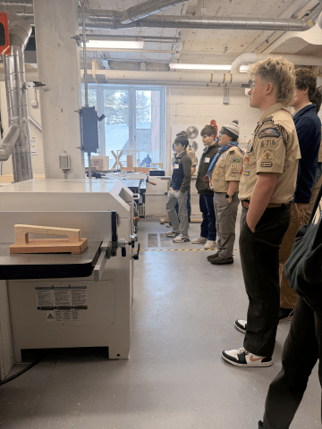 A group stands in a workshop facing machinery and workbenches with pipes and tools visible around the room.