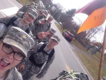 Group of Norwich cadets march in a line wearing camo uniform. Jessica Gnacke '16 appears in frame lower left.